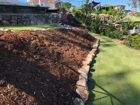 Freshly mulched garden bed with a curved timber sleeper edge meeting the lawn