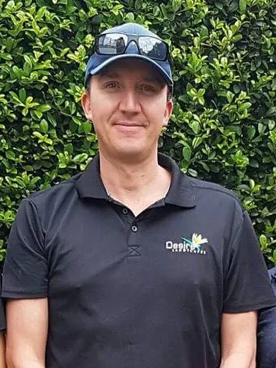Roger, founder of Desire Landscapes, in a cap and Desire Landscapes polo in front of a green hedge