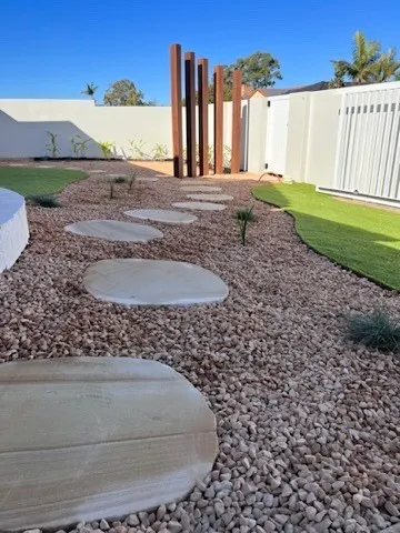 Sandstone stepping stones through river pebbles beside tall rusted steel garden posts