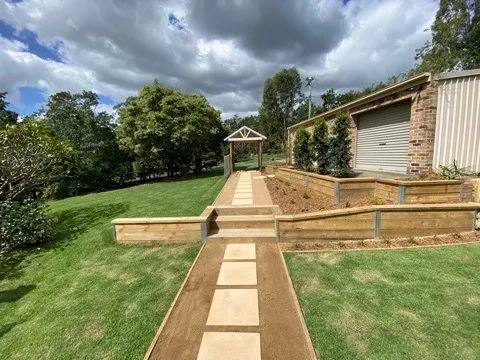 Long garden path flanked by terraced timber sleeper retaining walls leading to a brick home