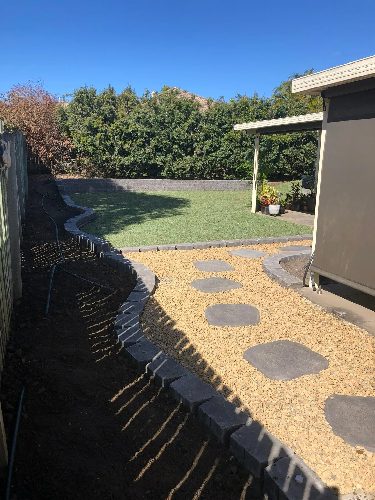 Curved garden path of dark stepping stones set in pale gravel beside a sleeper-edged garden bed