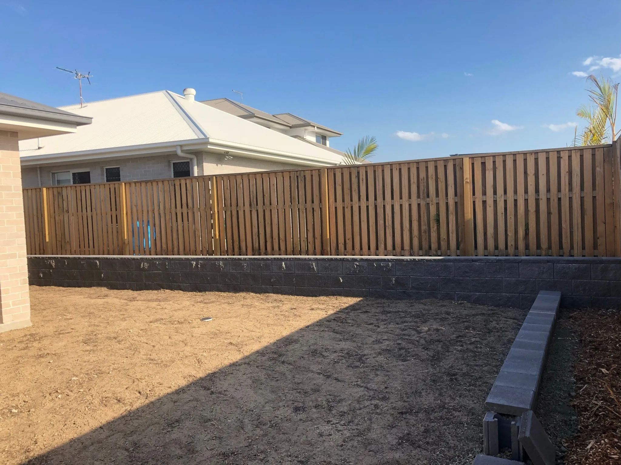 New timber paling fence above a concrete sleeper retaining wall on a new build, site prepared for turf