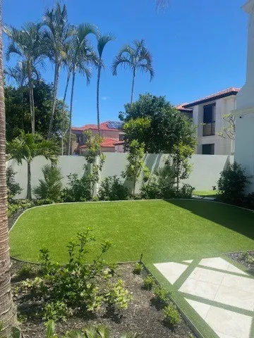 Townhouse courtyard with new lawn, garden beds and palms under a blue sky