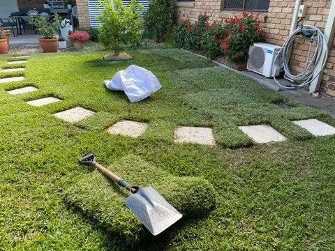 Turf being laid around square stepping pavers with a spade resting on the lawn